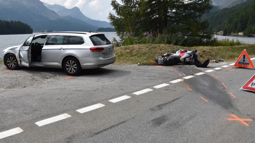 as Auto auf dem Ausstellplatz. Dahinter das am Boden liegende Motorrad. Im Hintergrund der Silser See (Foto: Kantonspolizei Graubünden).