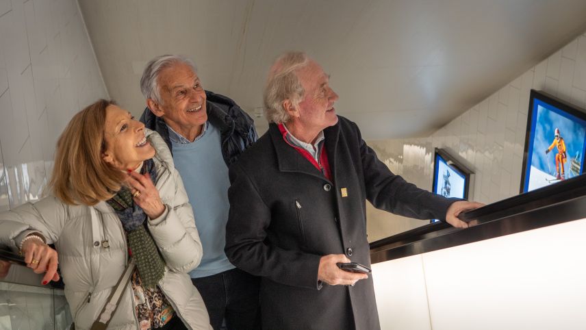 V.l: Annalisa und Werner Mattle passieren auf der Rolltreppe zusammen mit Martin Berthod die Ausstellung «Home of ­Championships» der Design Gallery und freuen sich ob so manchem Wiedererkennungseffekt. Foto: Jon Duschletta