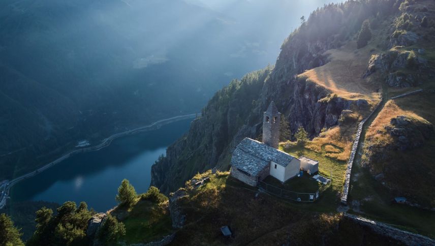 Blick auf die Kirche San Romerio in der Valposchiavo mit dem Lago di Poschiavo tief unten. Foto: Graubünden Ferien / Andri Flury