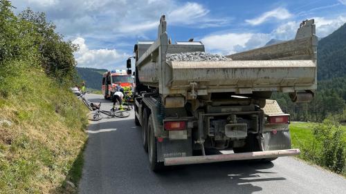 Der Lastwagen von hinten. Vor diesem ein Fahrrad am Boden und sowie Rettungskräfte und eine Ambulanz (Foto: Kantonspolizei Graubünden).