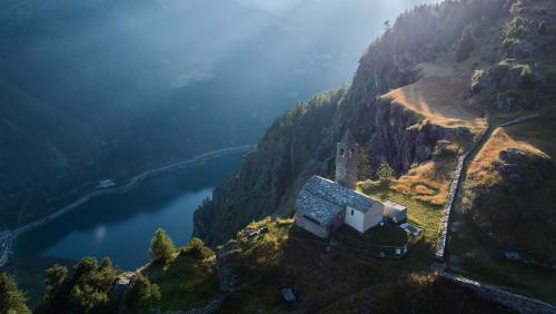 Blick auf die Kirche San Romerio in der Valposchiavo mit dem Lago di Poschiavo tief unten. Foto: Graubünden Ferien / Andri Flury